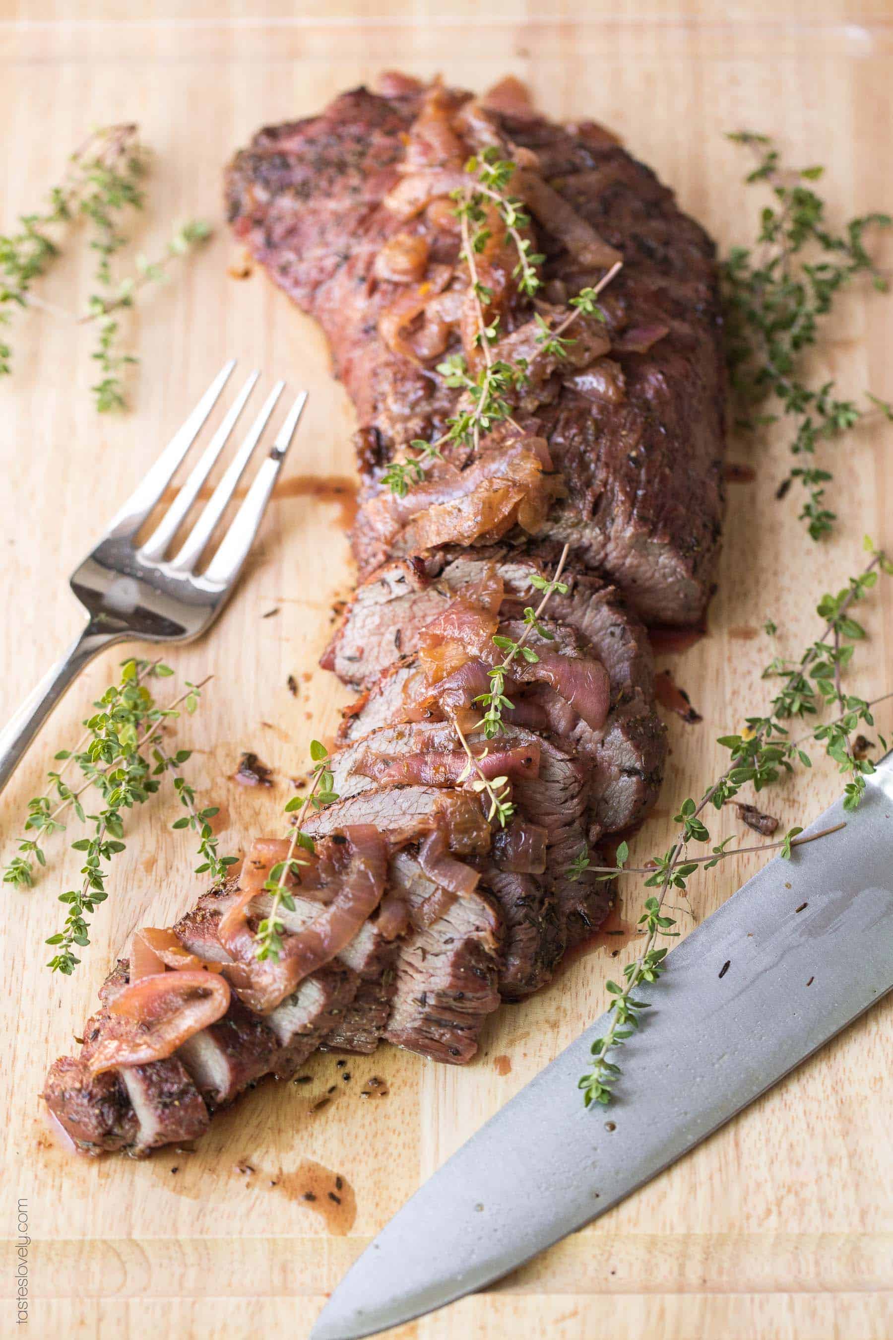 a cut of tri tip resting on a cutting board topped with fresh herbs