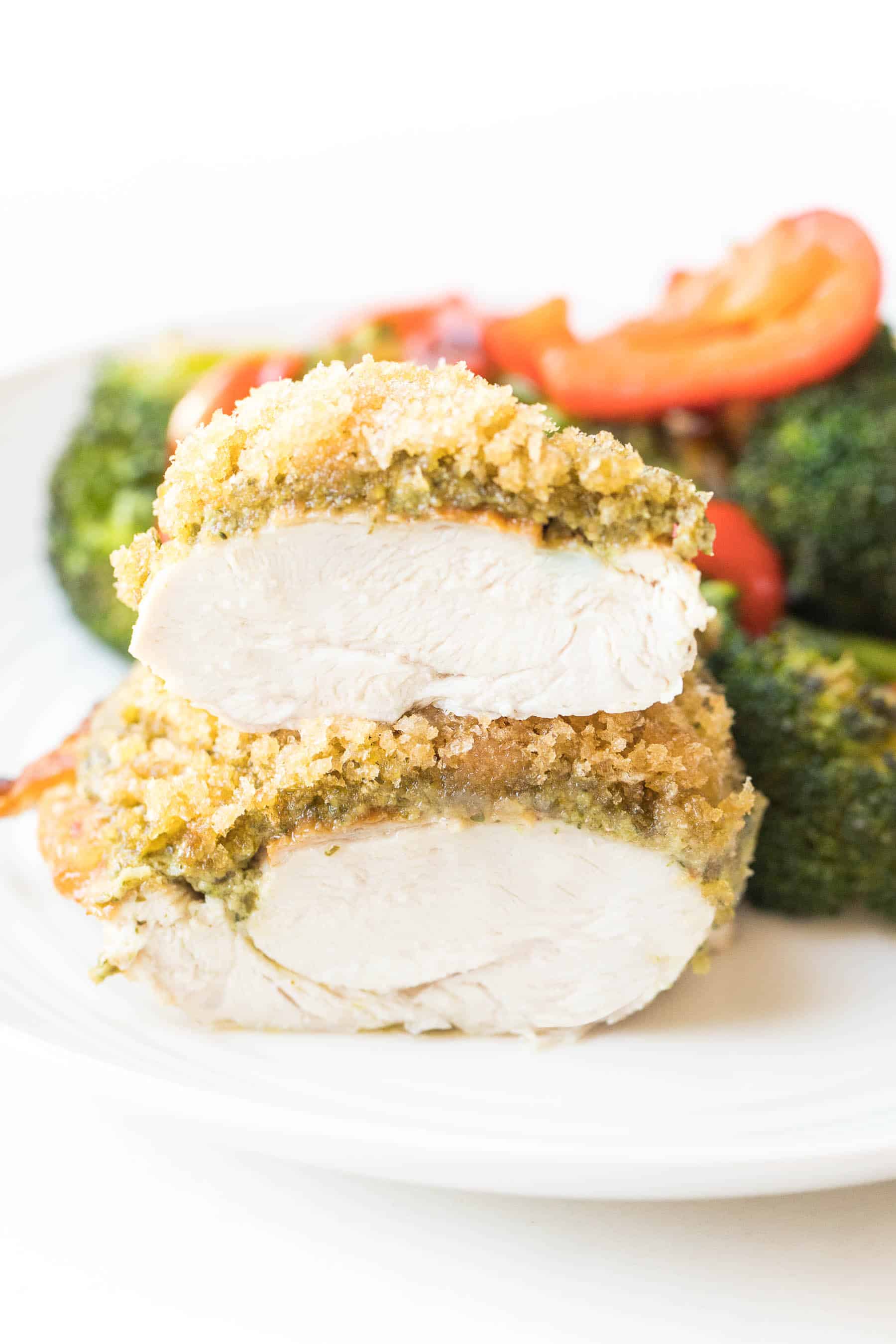 Crispy pesto chicken cut in half on a white plate