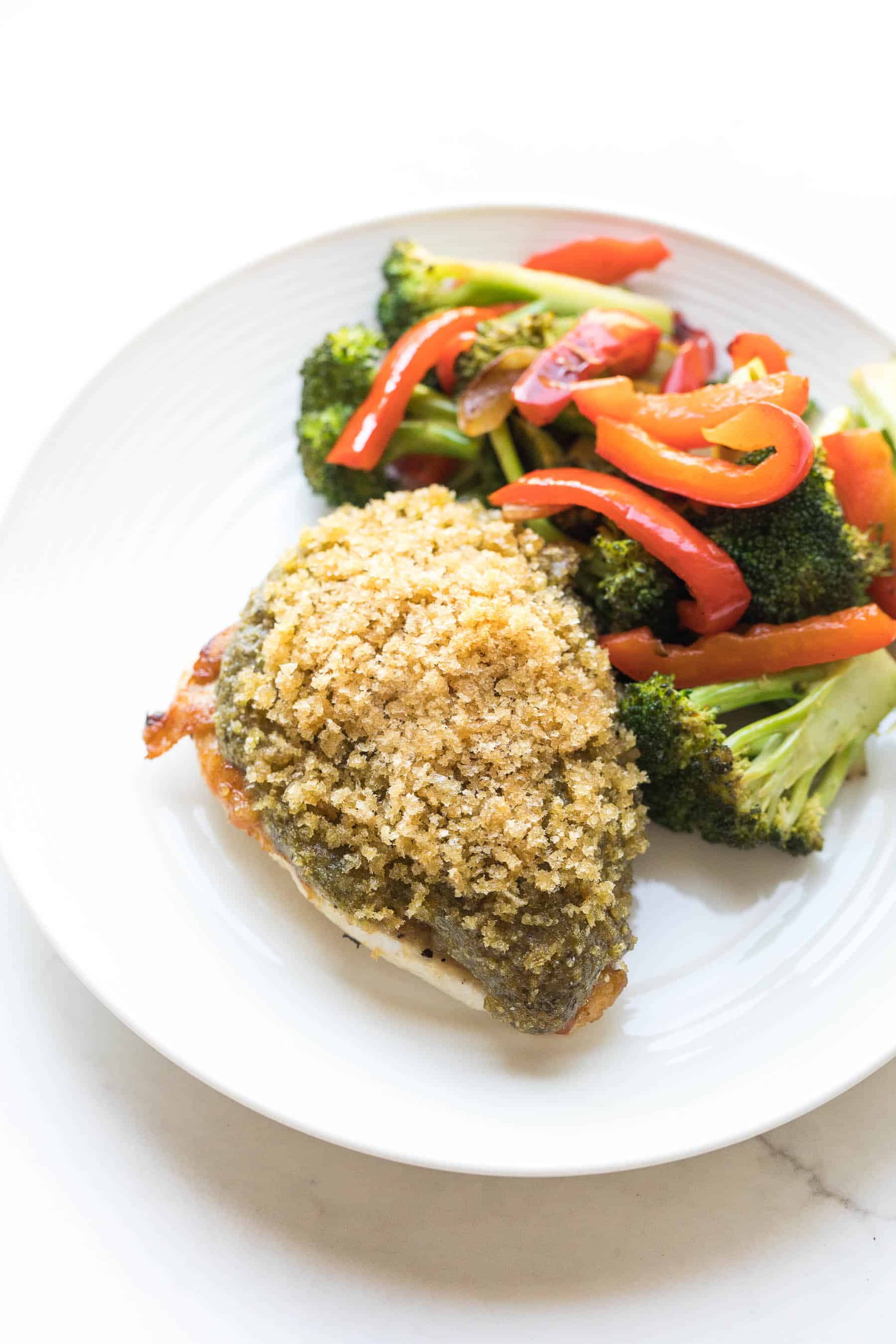 Crispy pesto chicken on a white plate with vegetables
