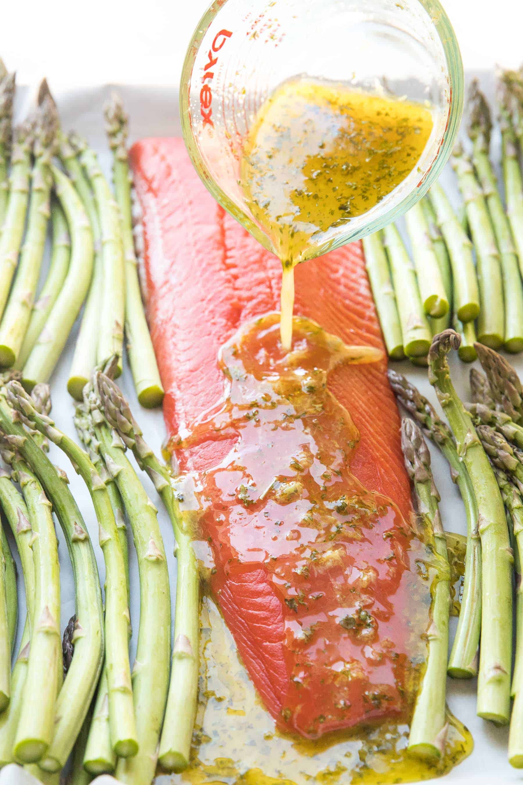 pouring marinade over sheet pan salmon and asparagus dinner