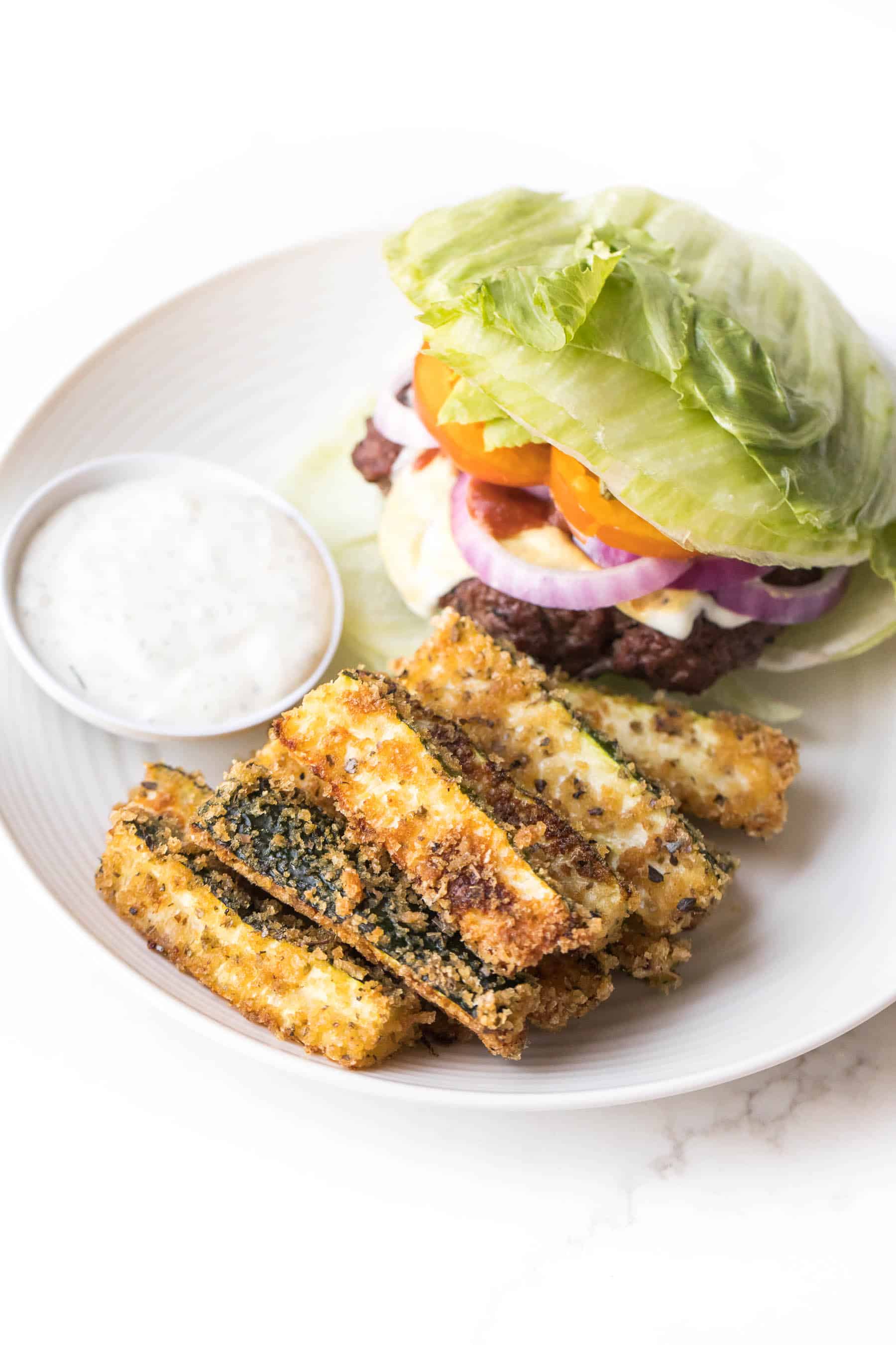 keto zucchini fries on a white plate with a burger and ranch dressing on a white background