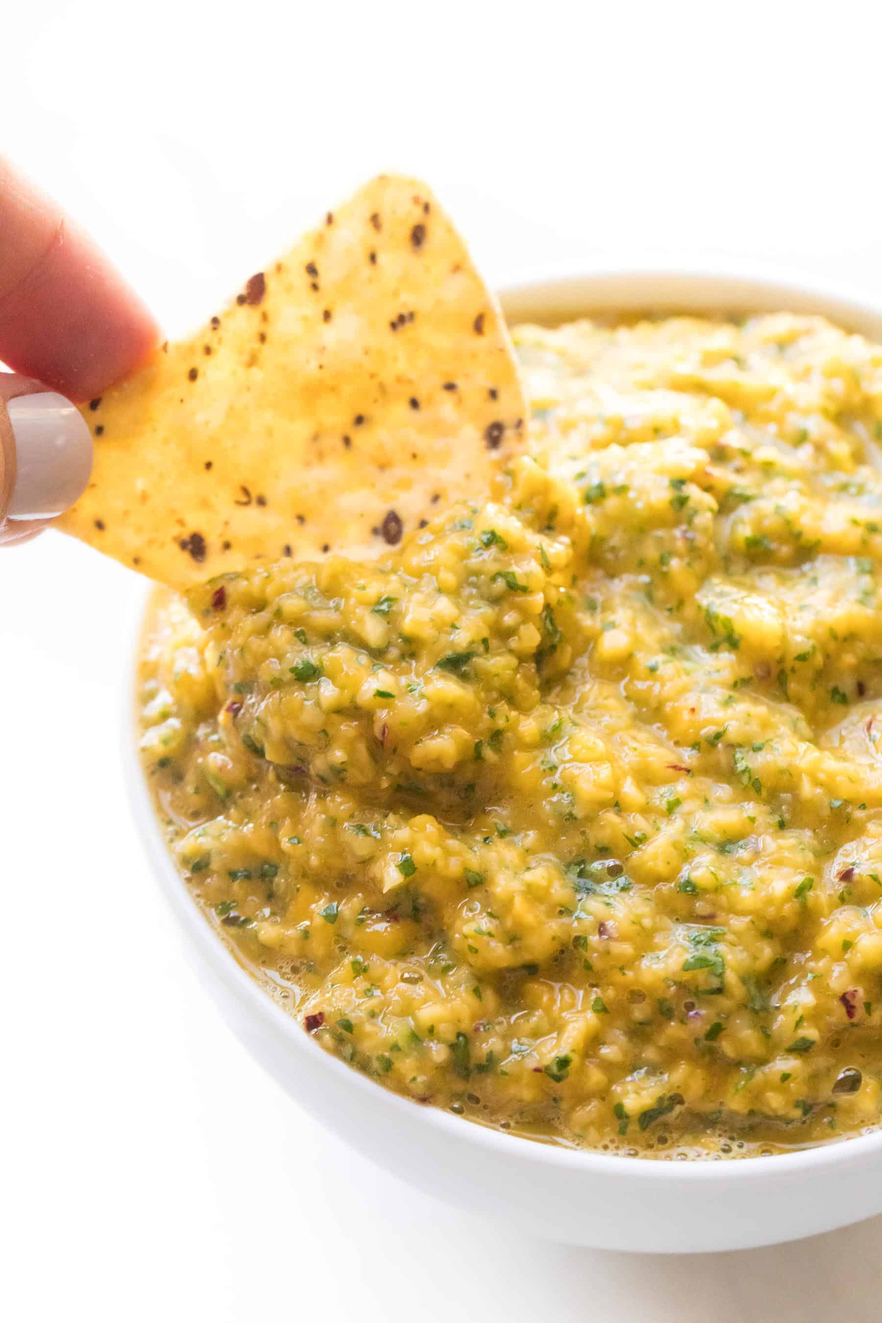 hand dipping a chip into mango salsa on a white background