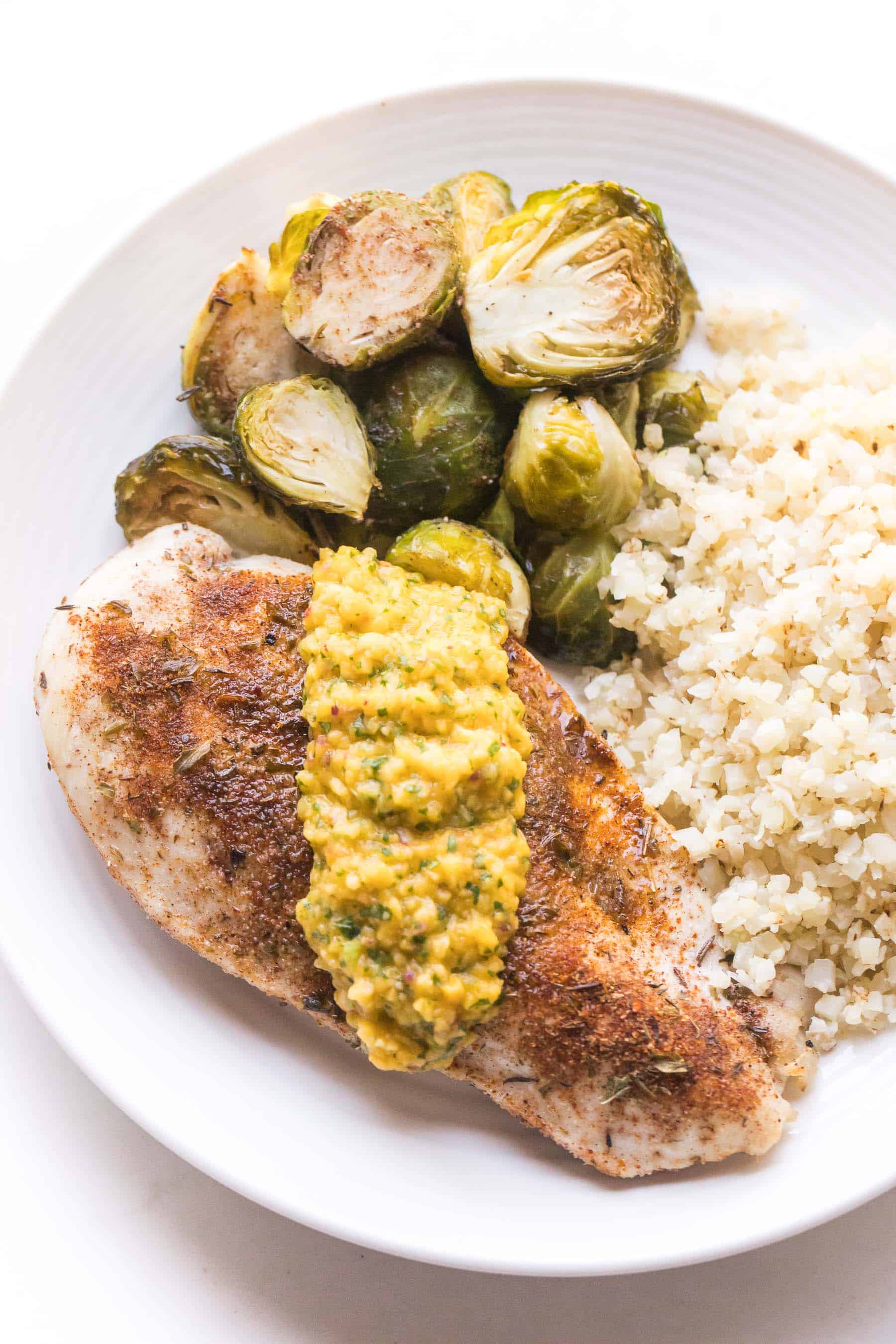 jamaican chicken topped with mango salsa with brussles sprouts and cauliflower rice on a white plate