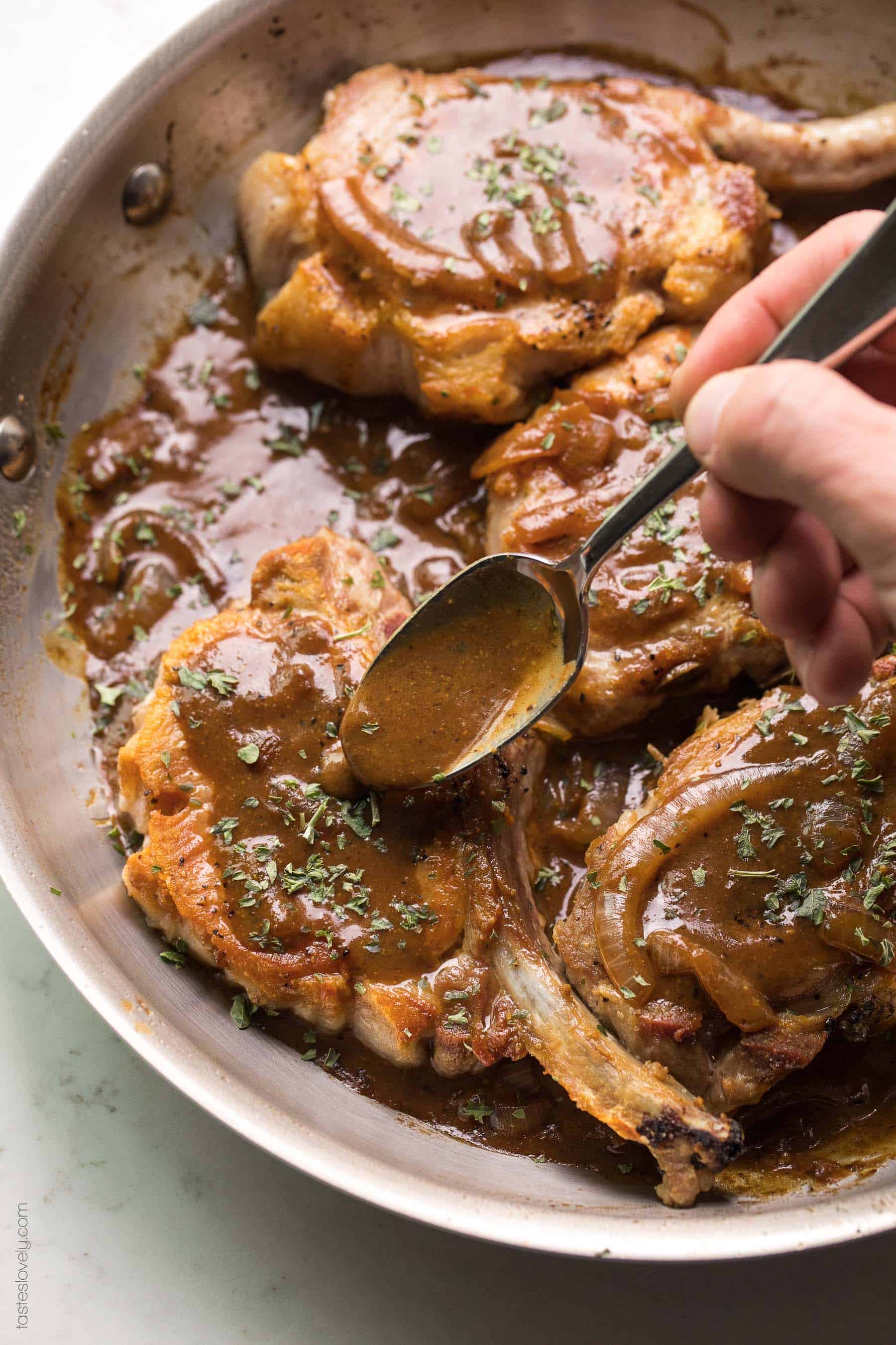 Spooning brown balsamic msutard sauce over pork chops in a skillet