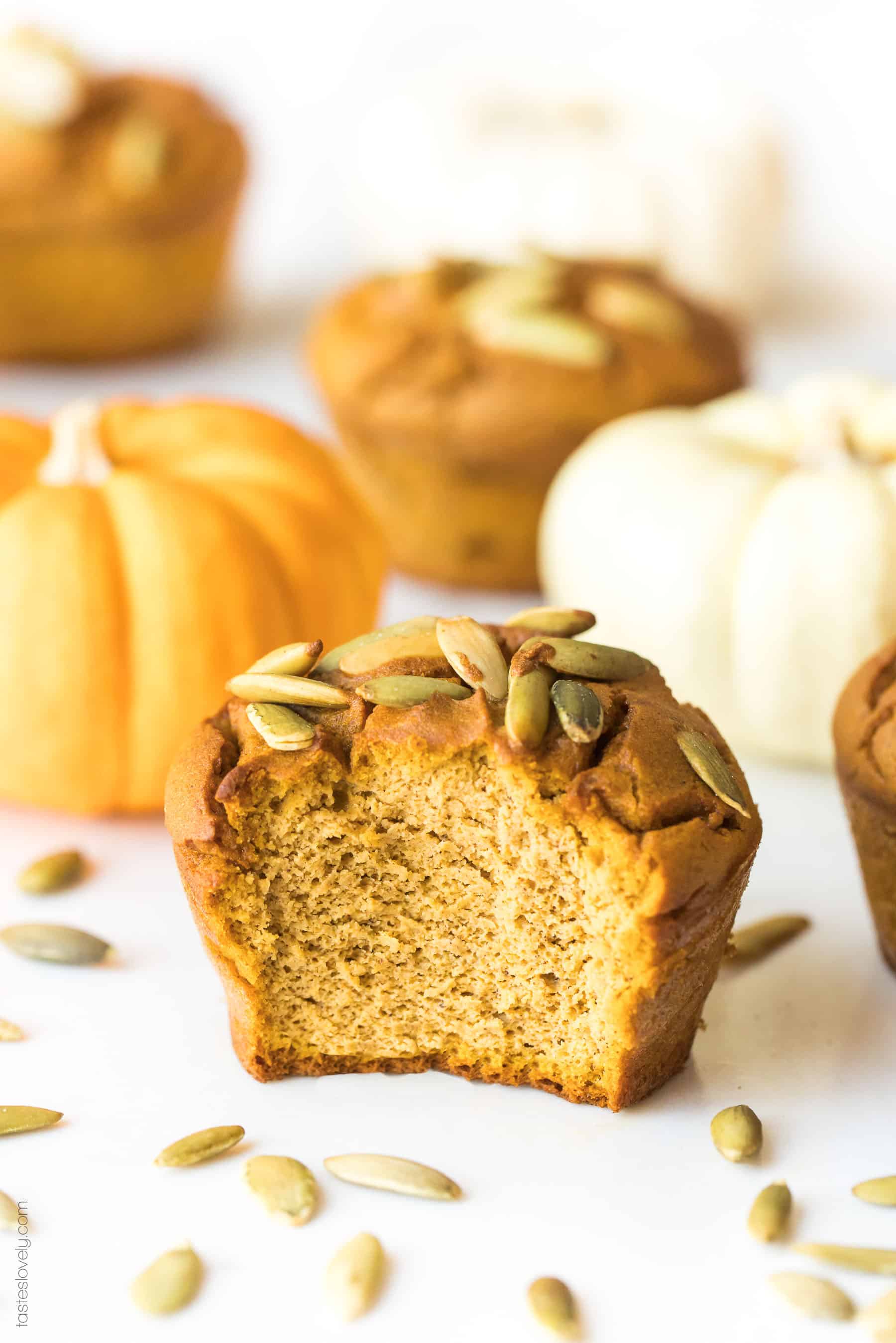 A almond flour pumpkin muffin with a bite taken out of it with small pumpkins in the background