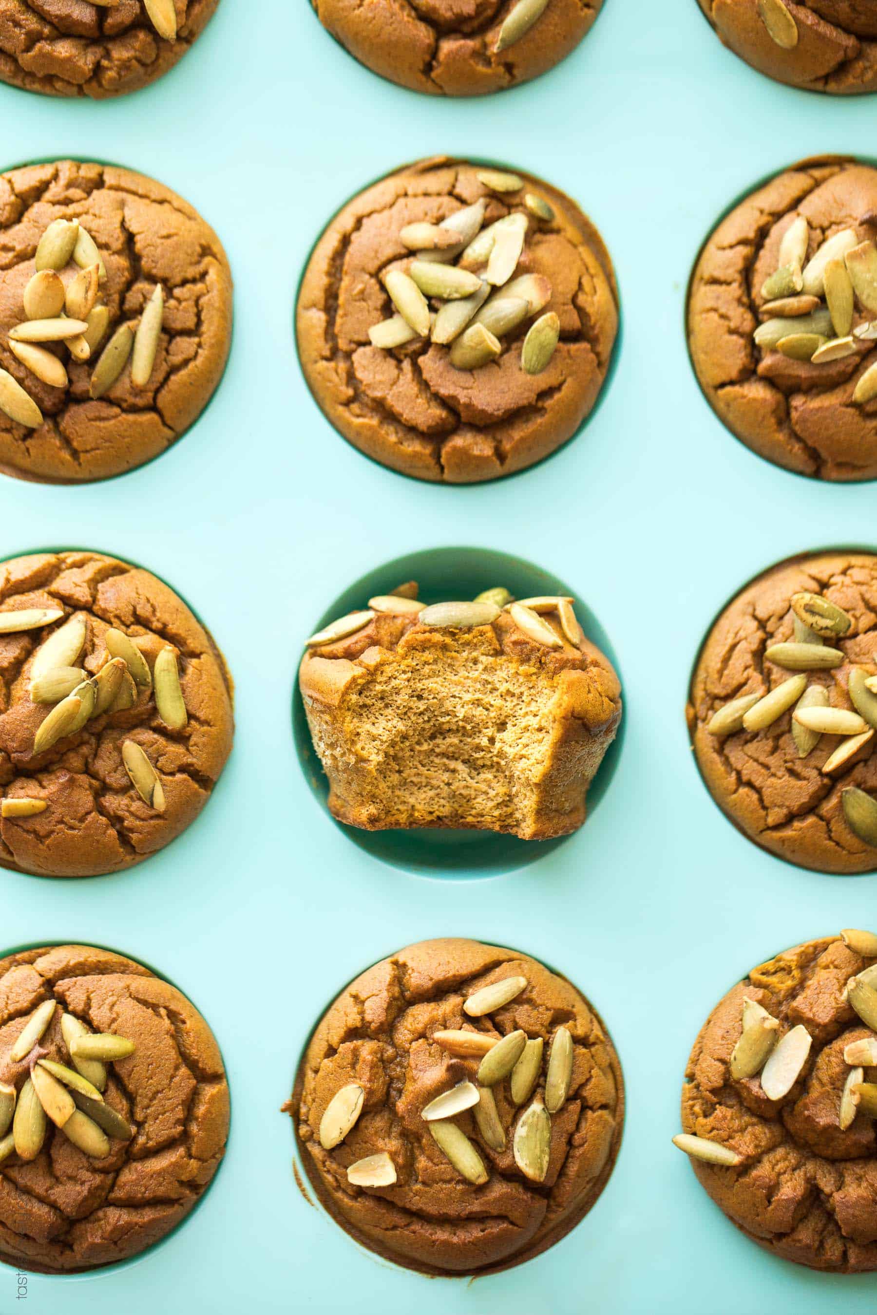 A tray of paleo pumpkin muffins with 1 muffin flipped up with a bite taken out of it