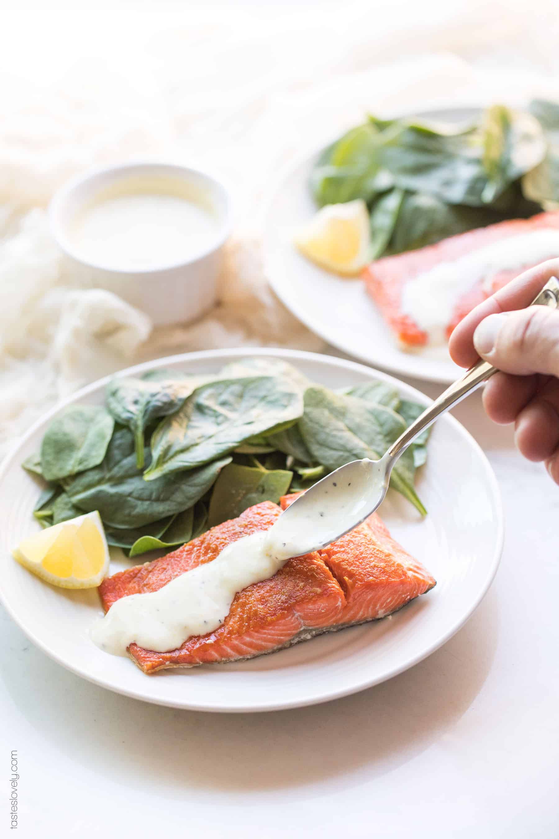 Pouring lemon garlic aioli over salmon on a plate with spinach