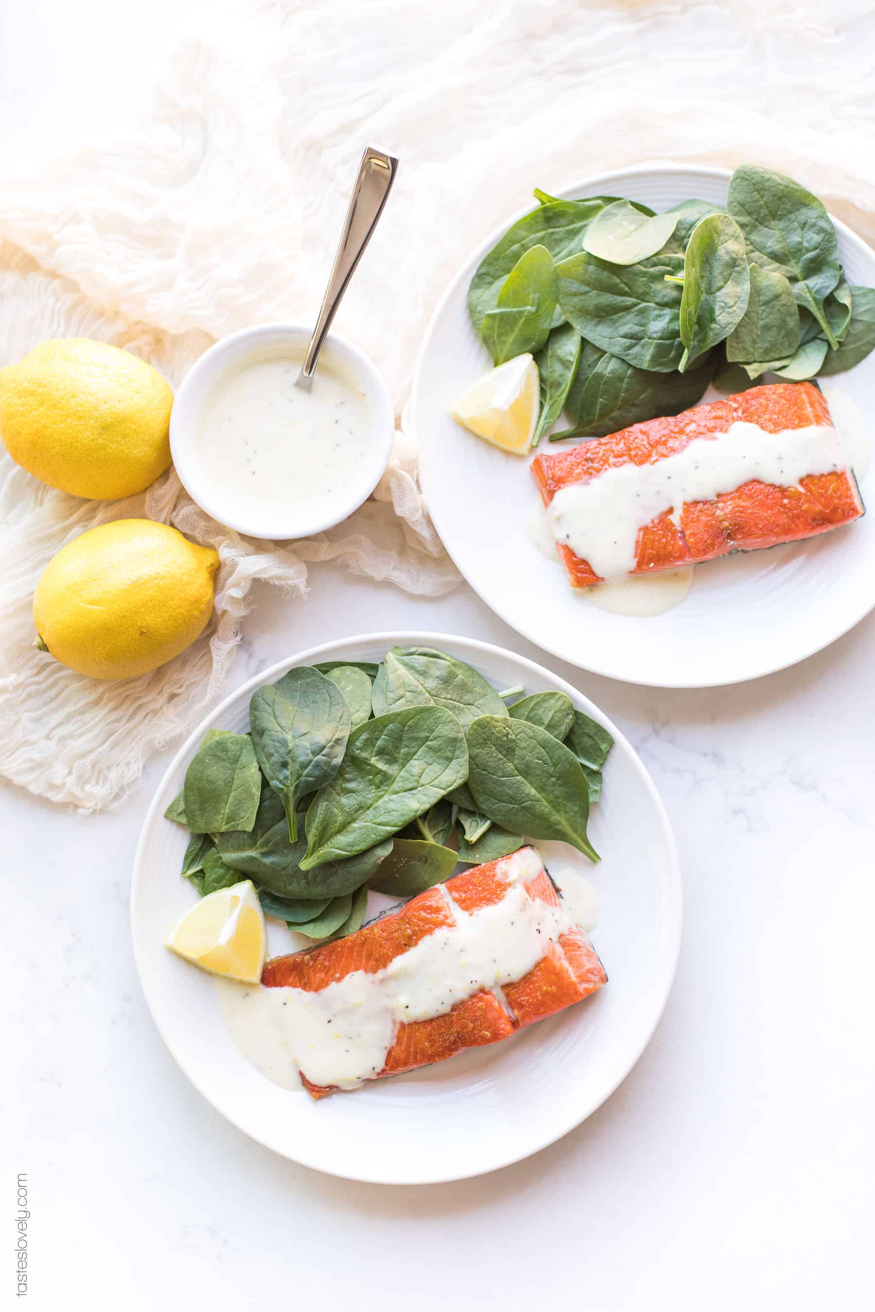 Salmon topped with a white sauce lemon garlic aioli on a plate with spinach