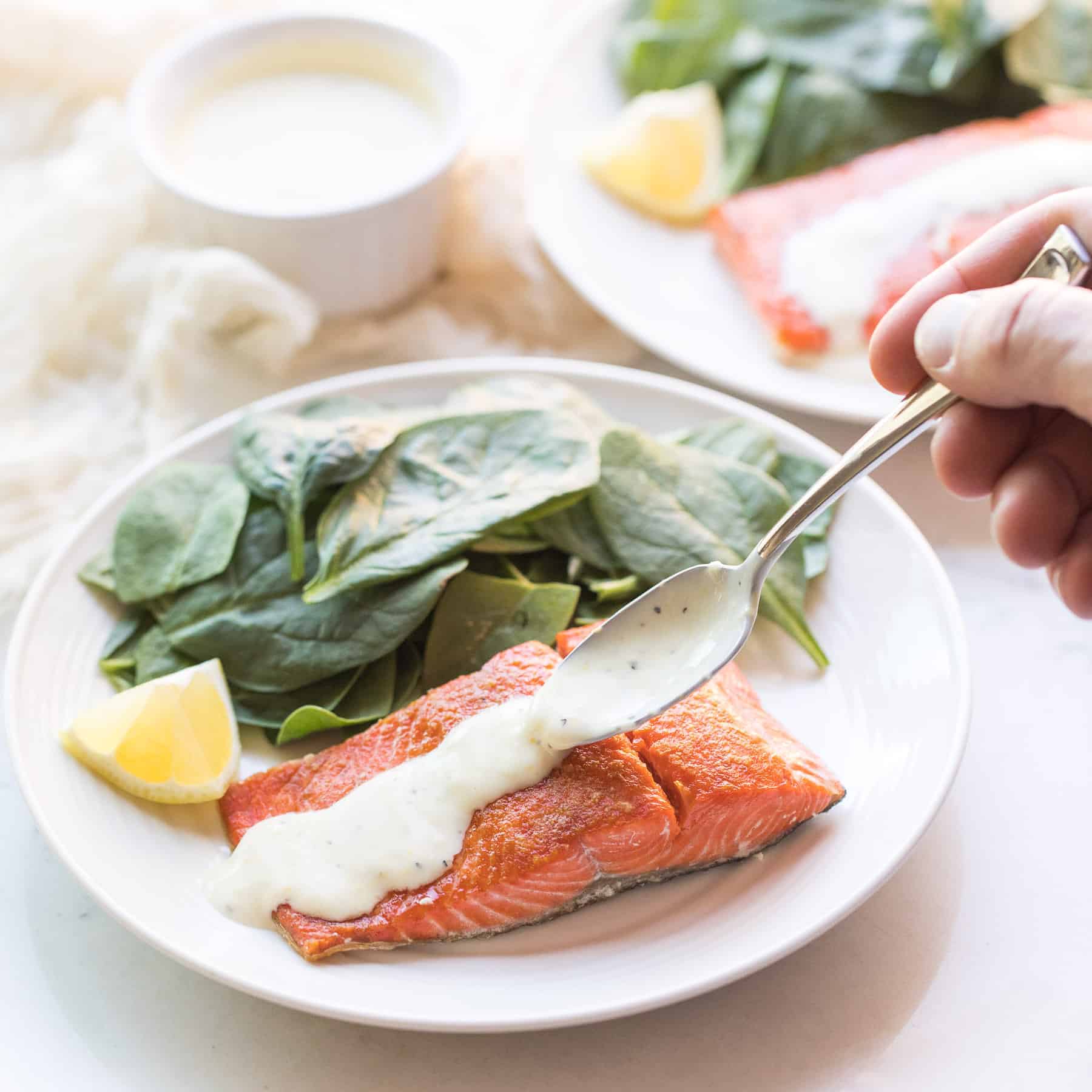 spinach and salmon on a white plate with a spoon drizzling sauce