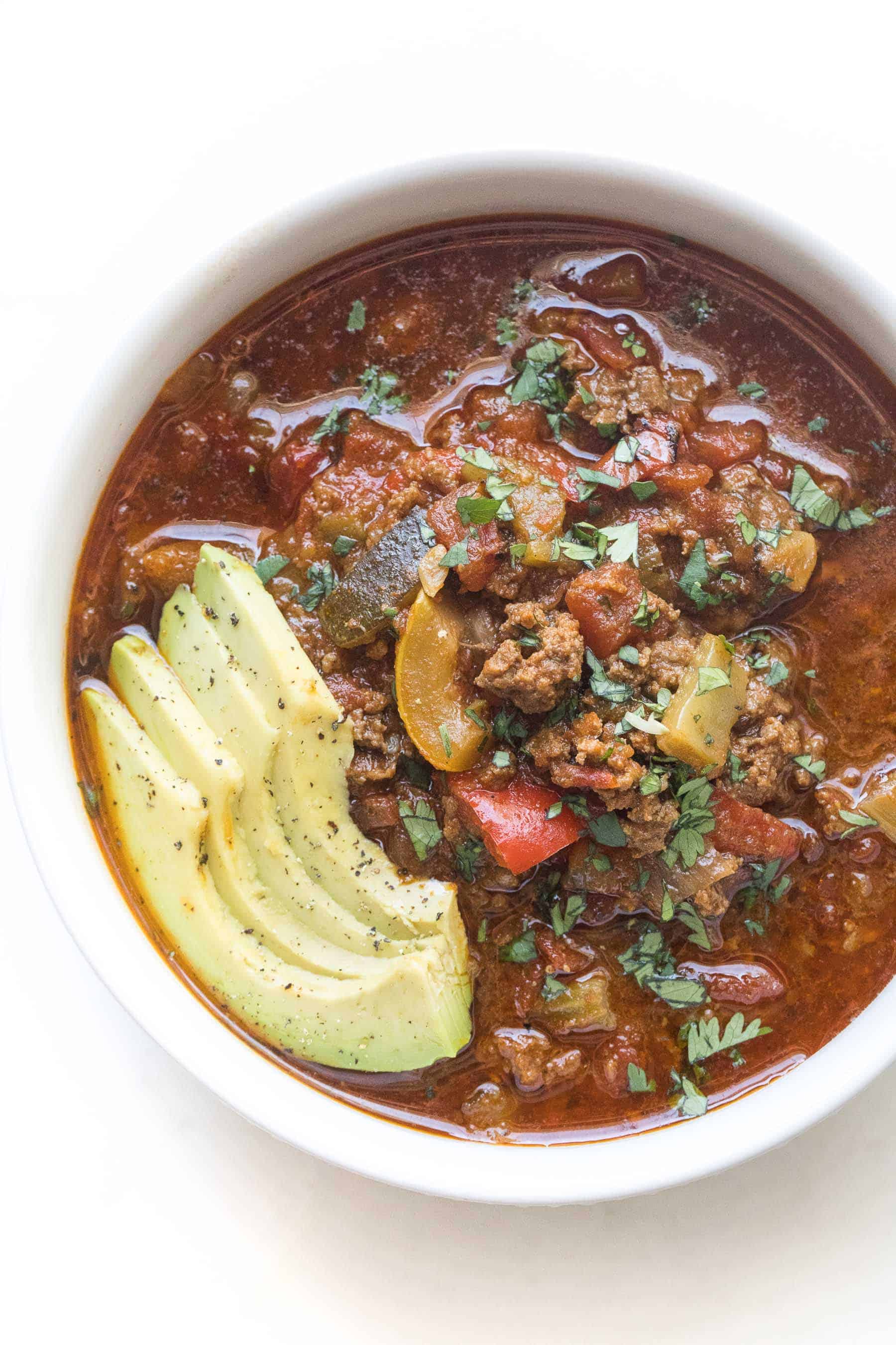 beef chili in a white bowl on a white background with avocado and cilantro