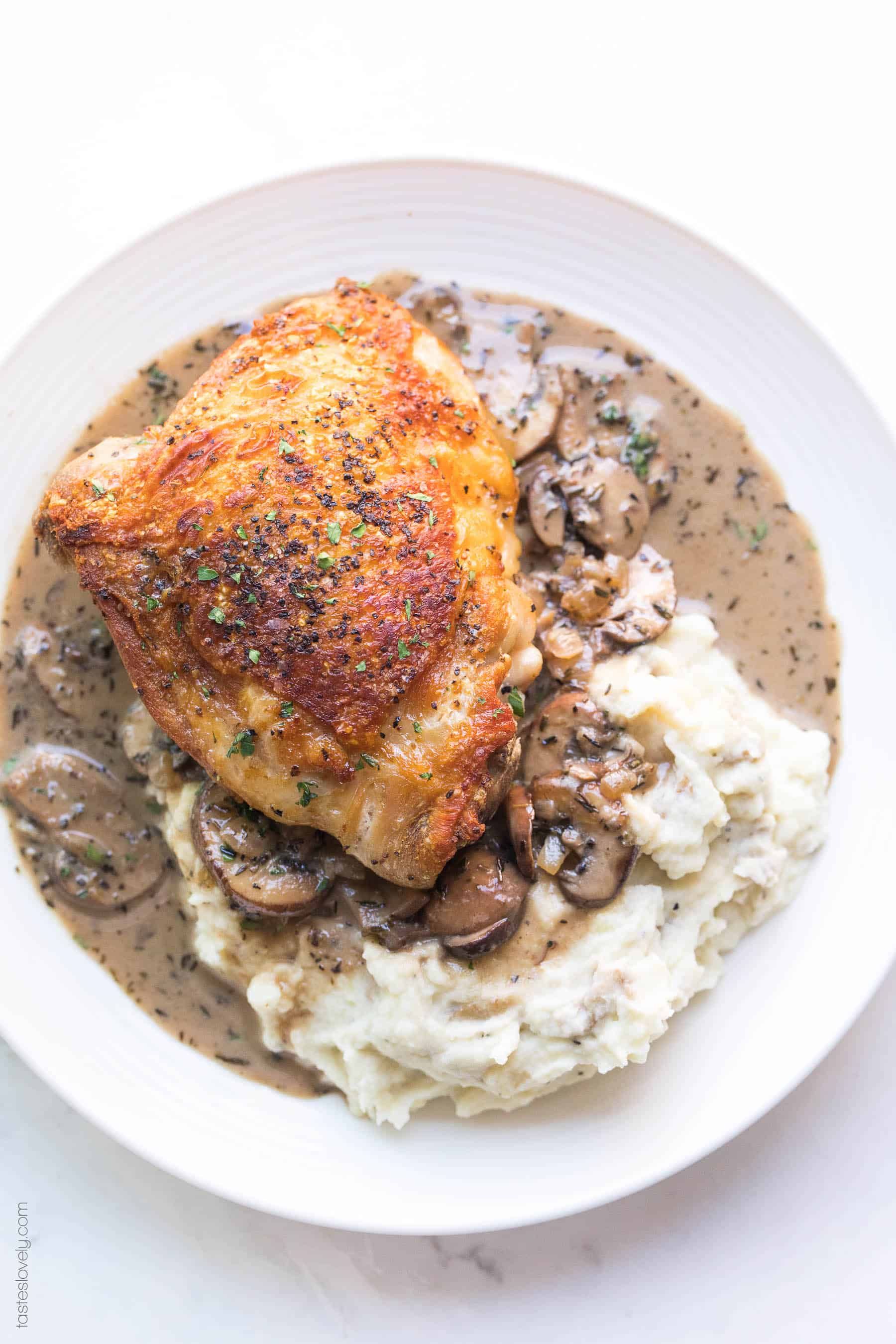 Crispy chicken thighs on a plate with mashed potatoes and creamy mushroom sauce