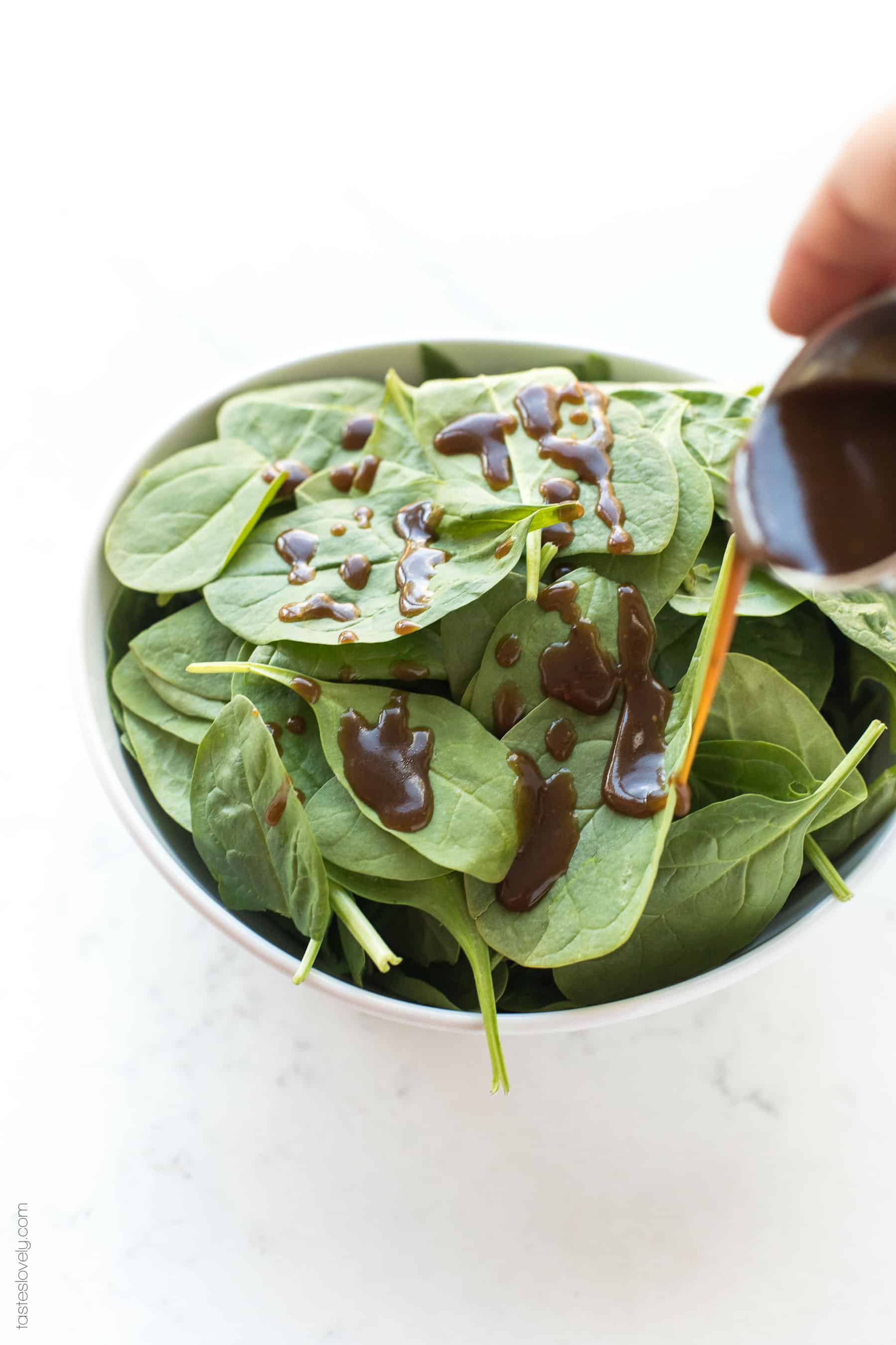 drizzling balsamic vinaigrette salad dressing on spinach leaves