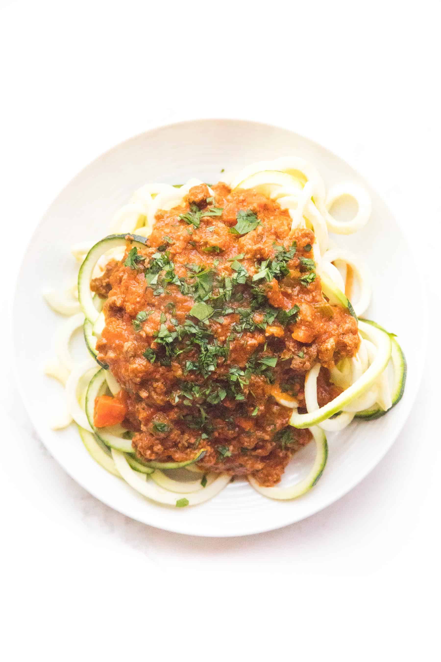 Zucchini noodles with red bolognese sauce on a white plate and background