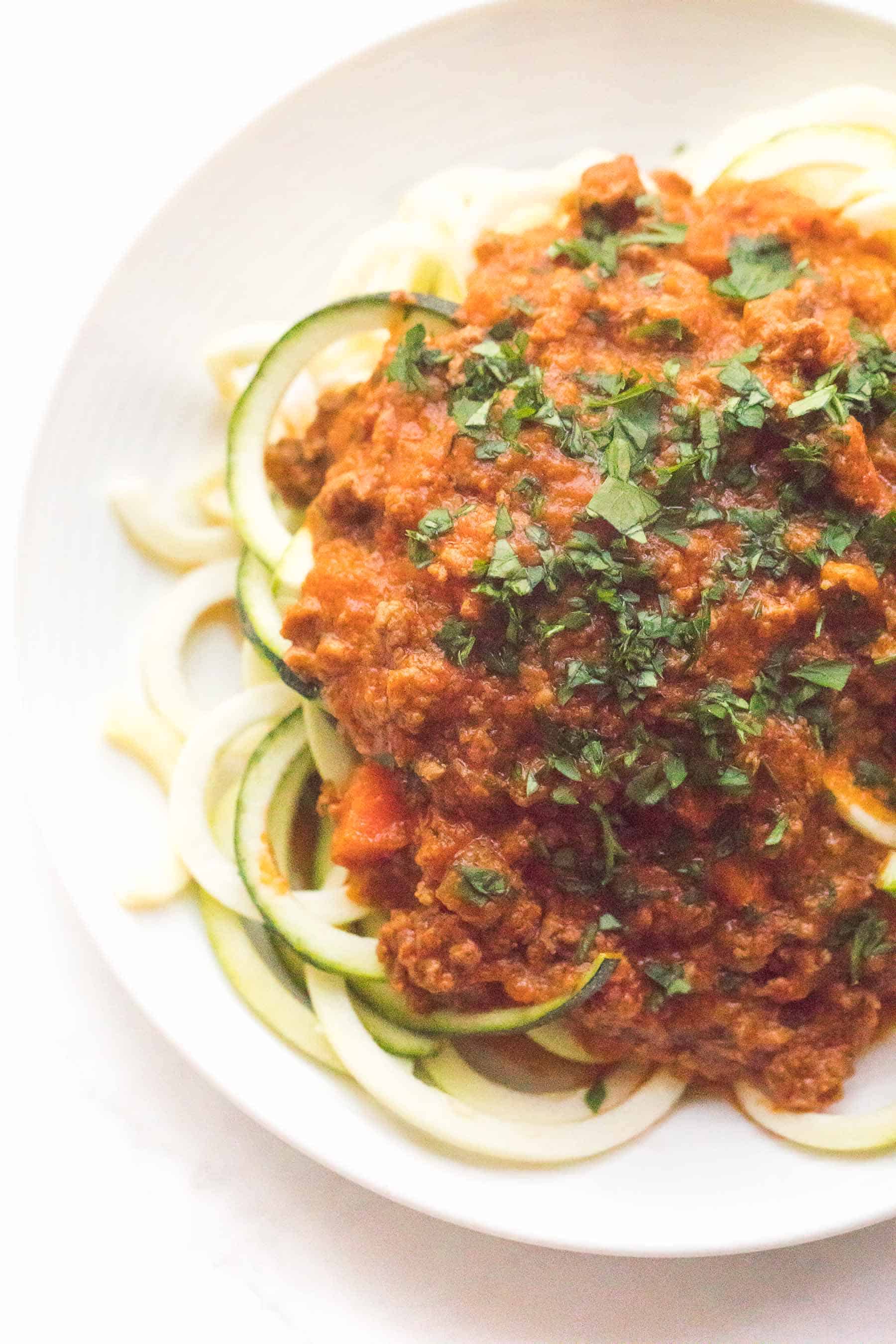 Zucchini noodles with red bolognese sauce on a white plate and background