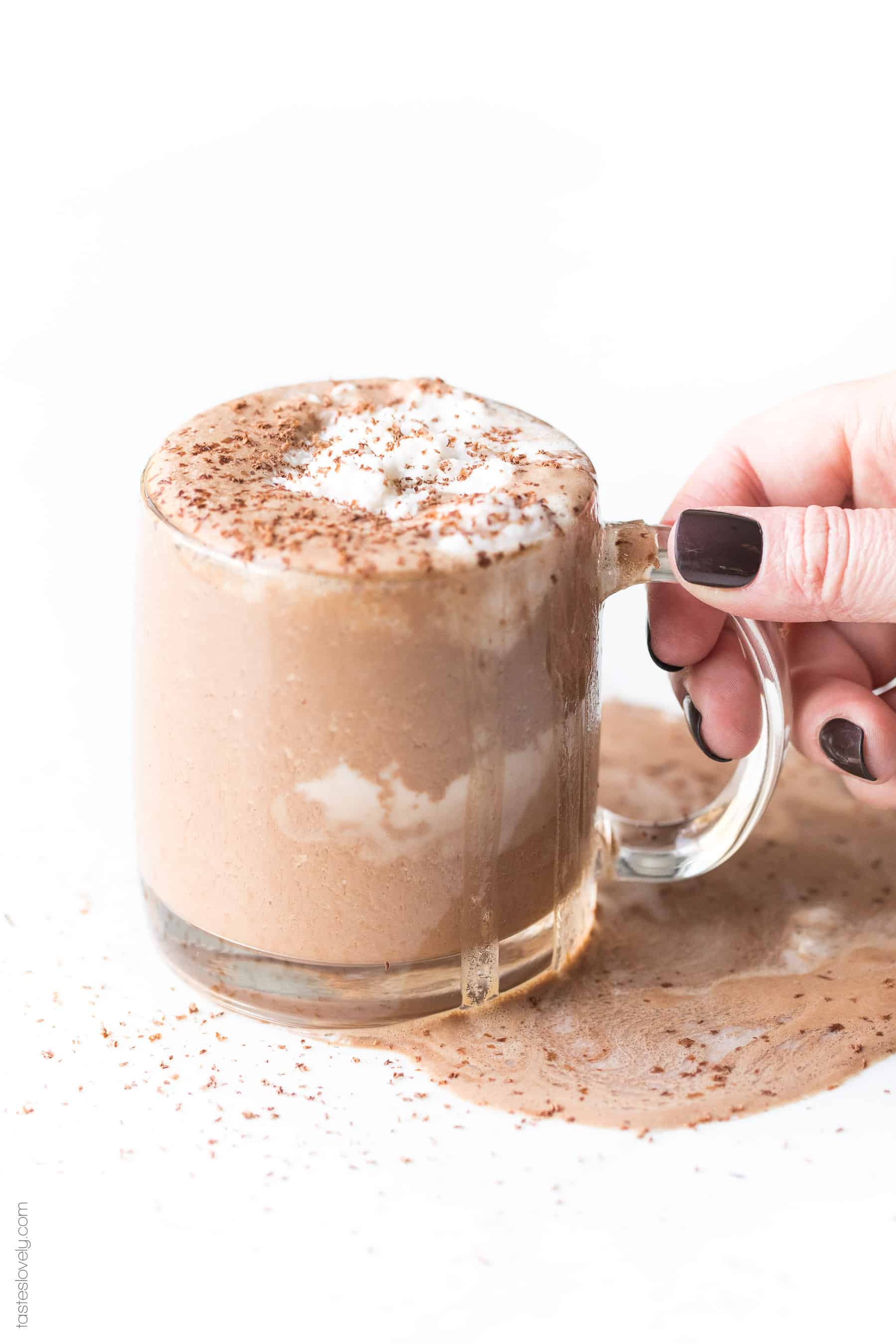 Hand holding hot chocolate in a clear mug topped with whipped cream and shaved chocolate