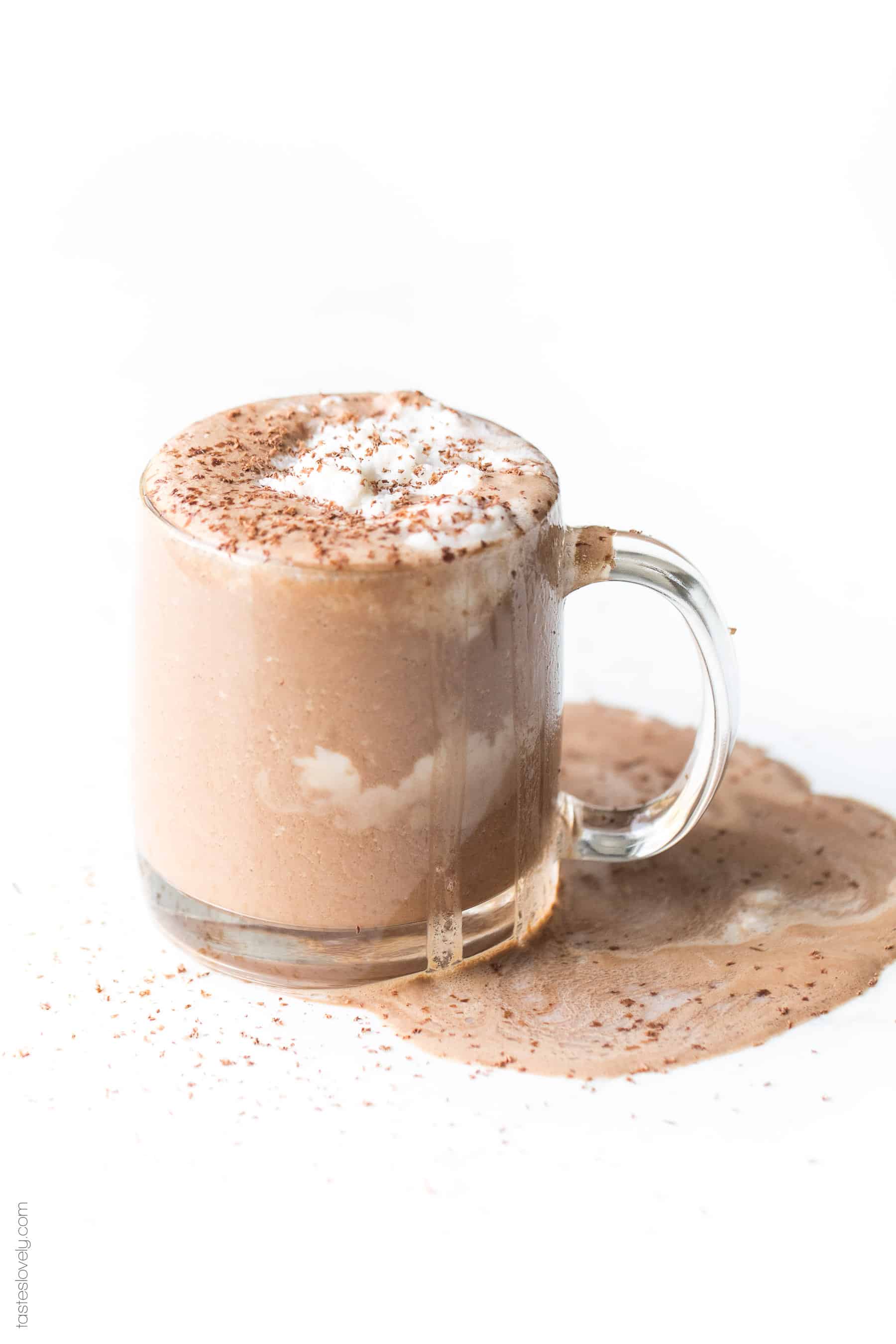 a clear mug filled with hot cocoa and topped with whipped cream and shaved chocolate