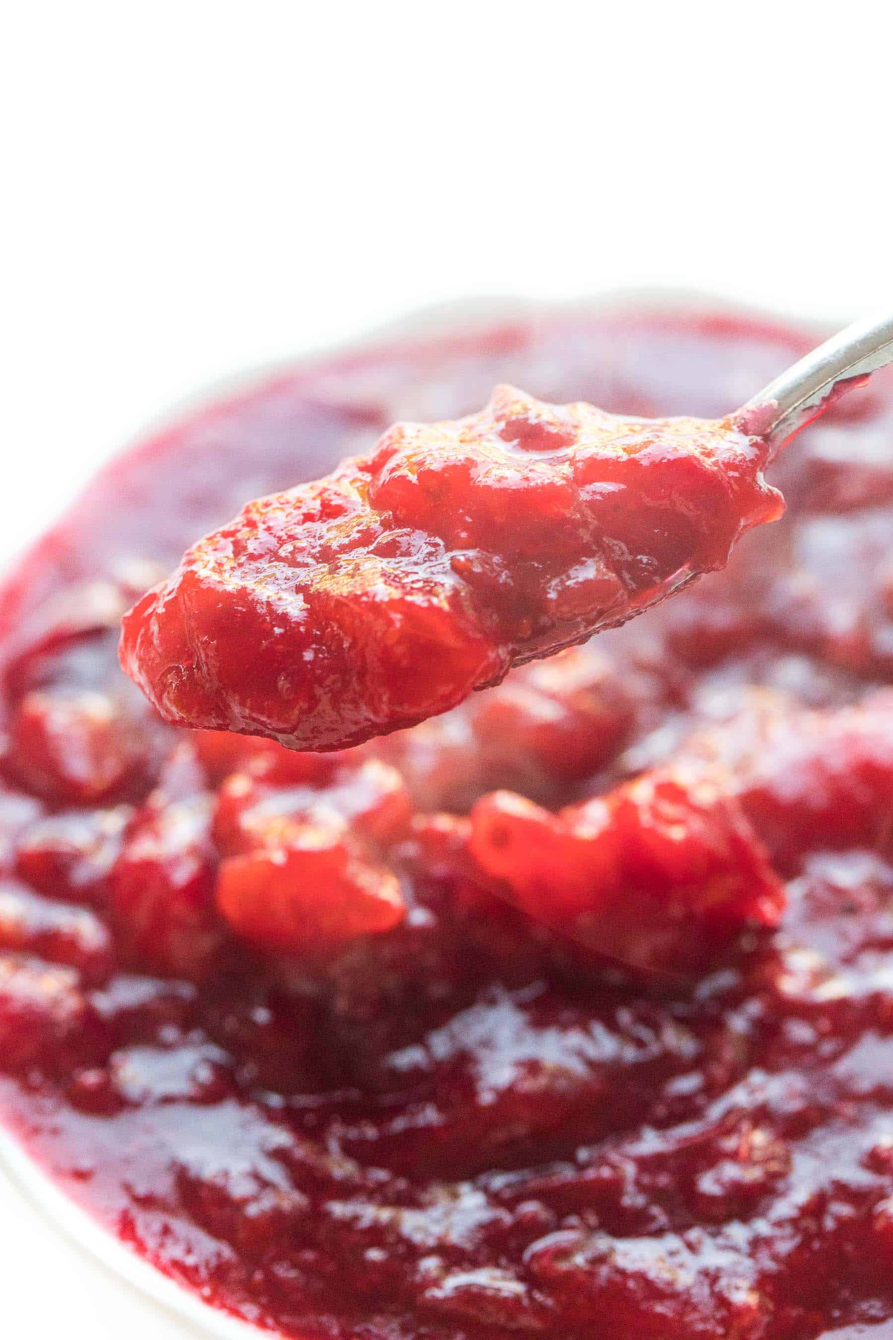 spoon dripping cranberry sauce in a white bowl