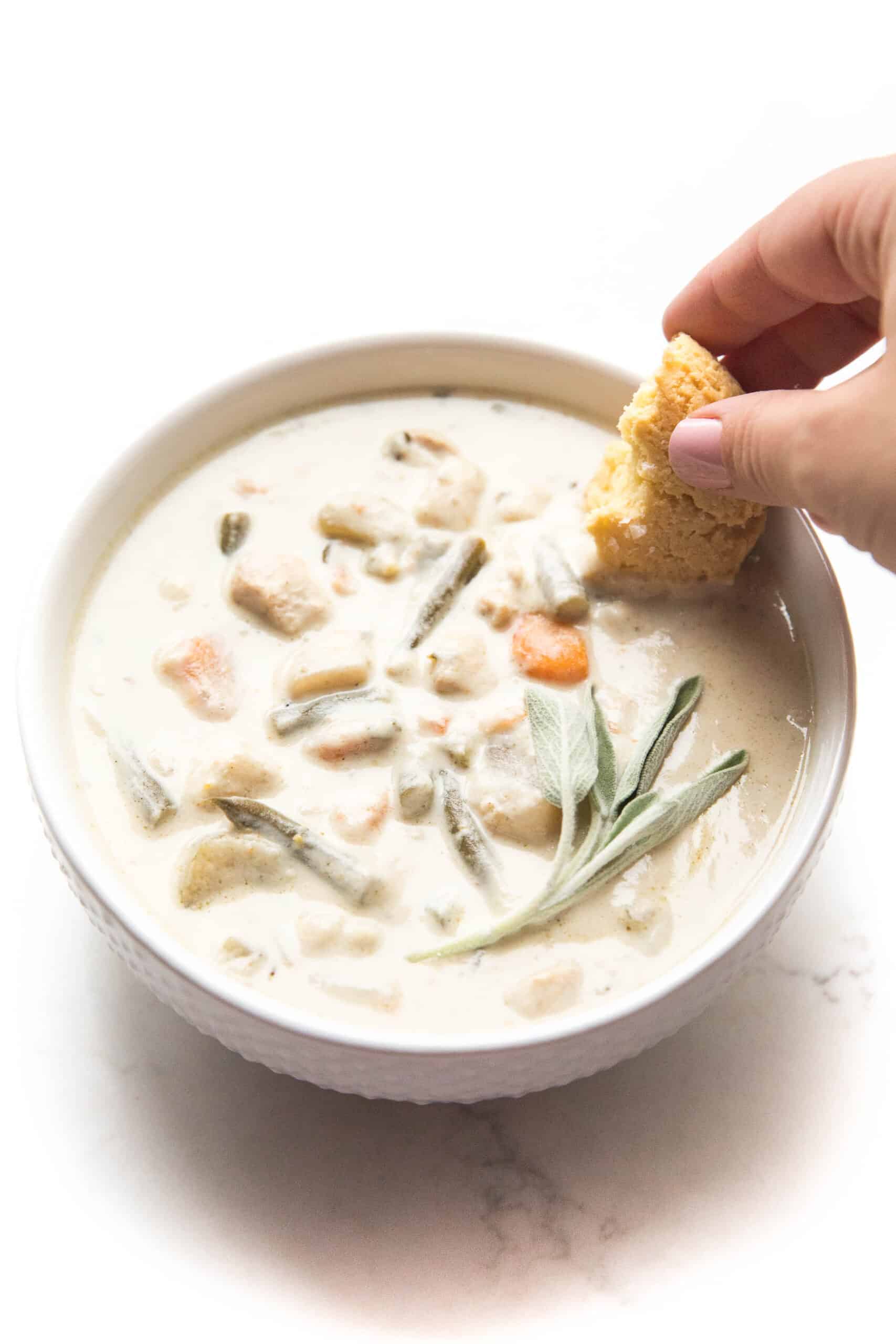 dipping a keto biscuit in creamy chicken chowder in a white bowl + background