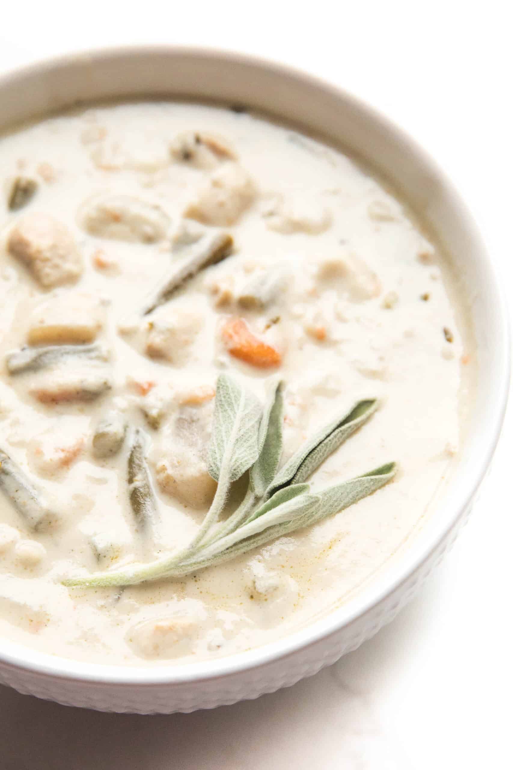 chicken chowder in a white bowl with fresh sage garnish on top