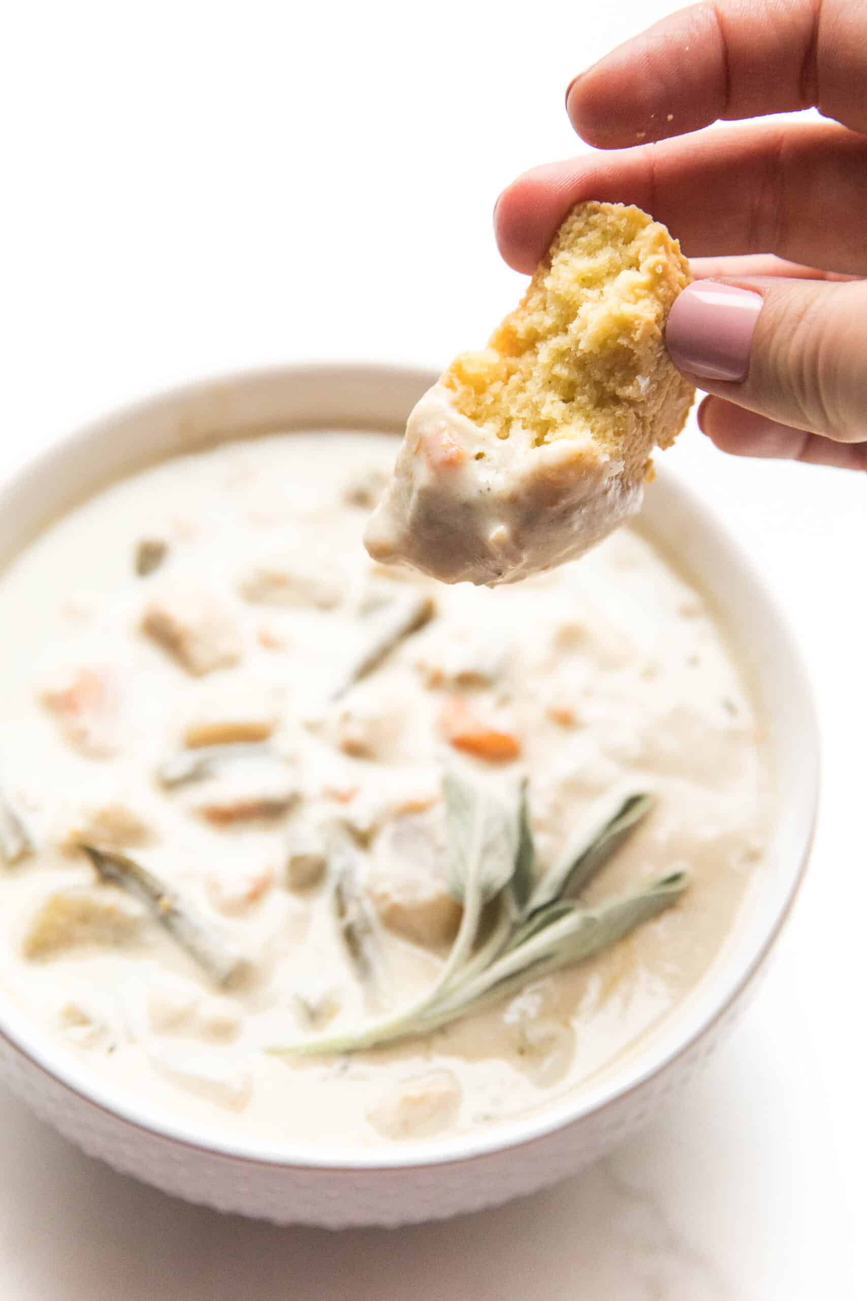 dipping a keto biscuit in creamy chicken chowder in a white bowl + background