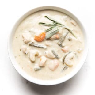 creamy chicken chowder in a white bowl and background with sage garnish on top