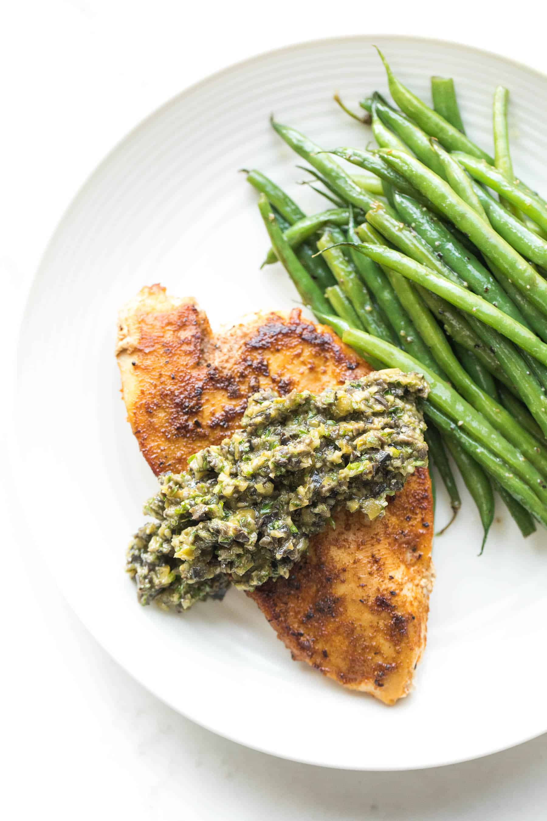 Chicken with olive tapenade and green beans on a white plate