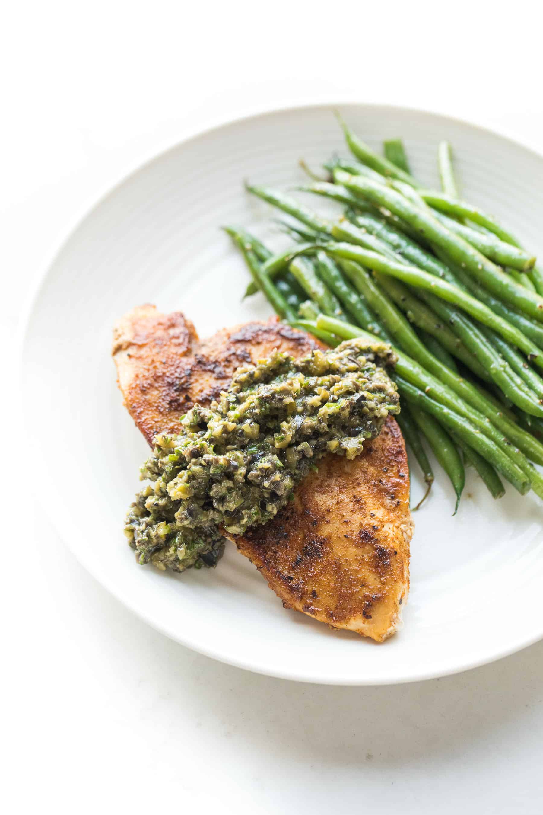 Chicken with olive tapenade and green beans on a white plate