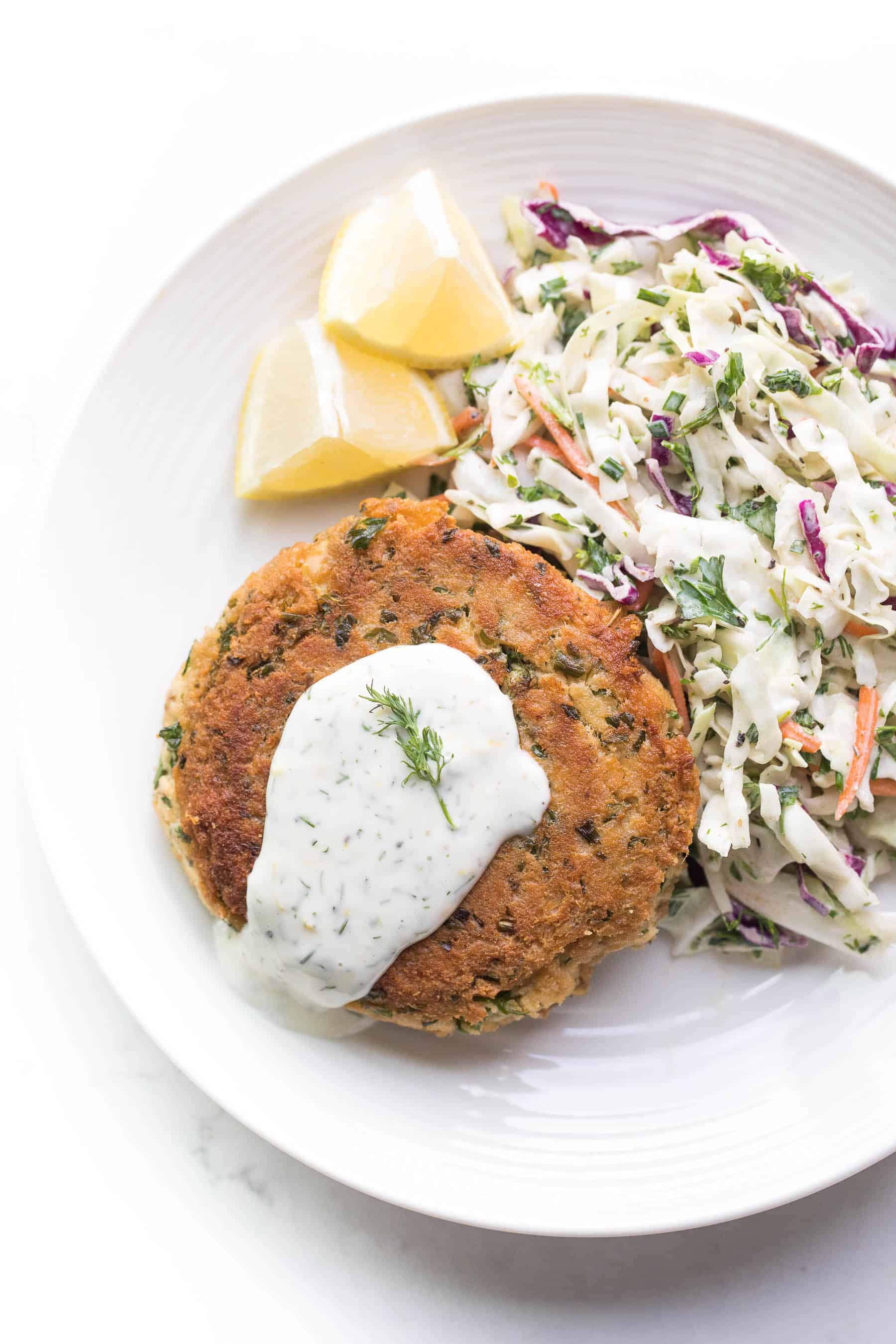 Salmon patty on a white plate with coleslaw and lemon wedges