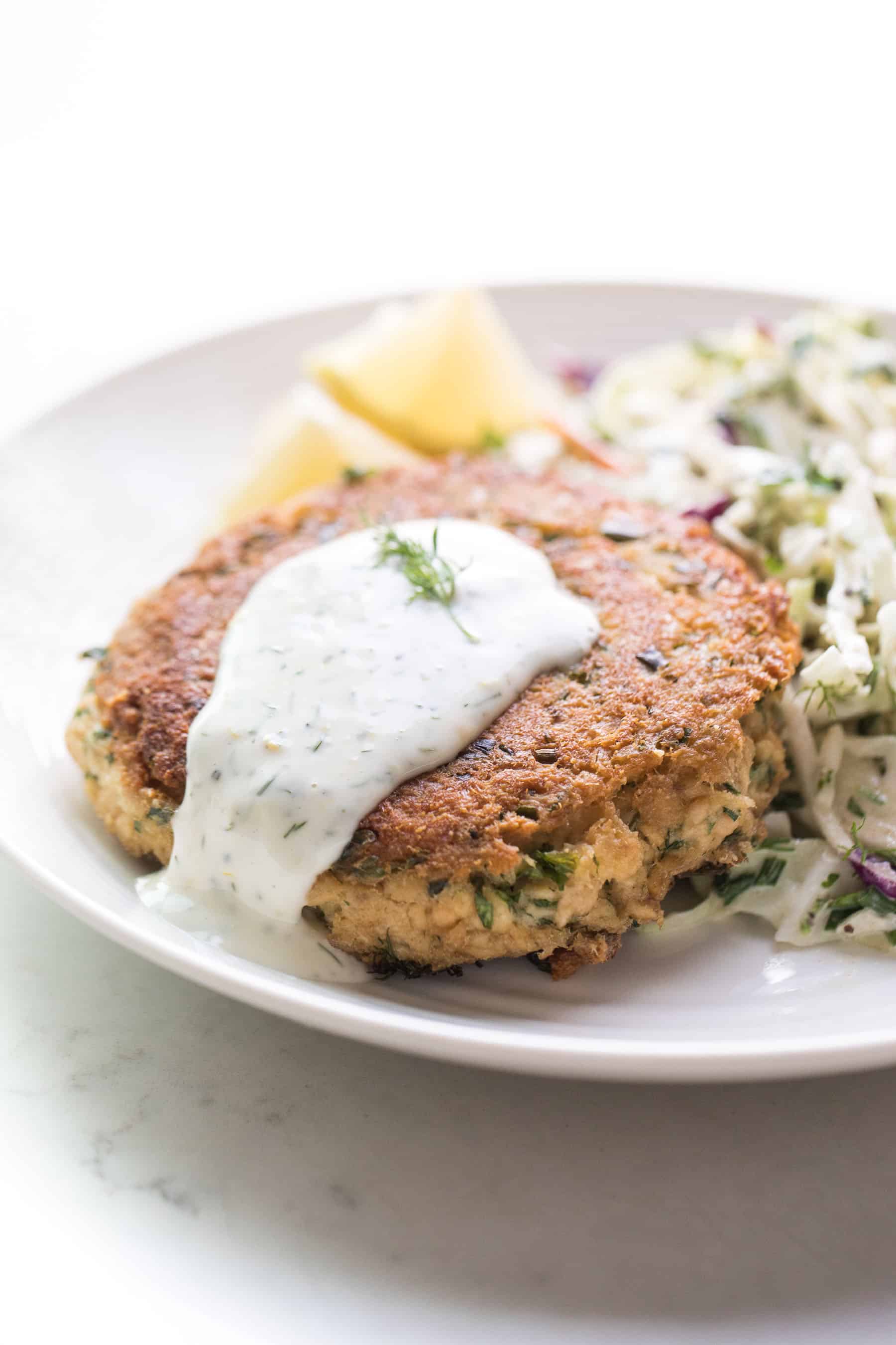 Salmon patties on a white plate with aioli, coleslaw and lemon wedges