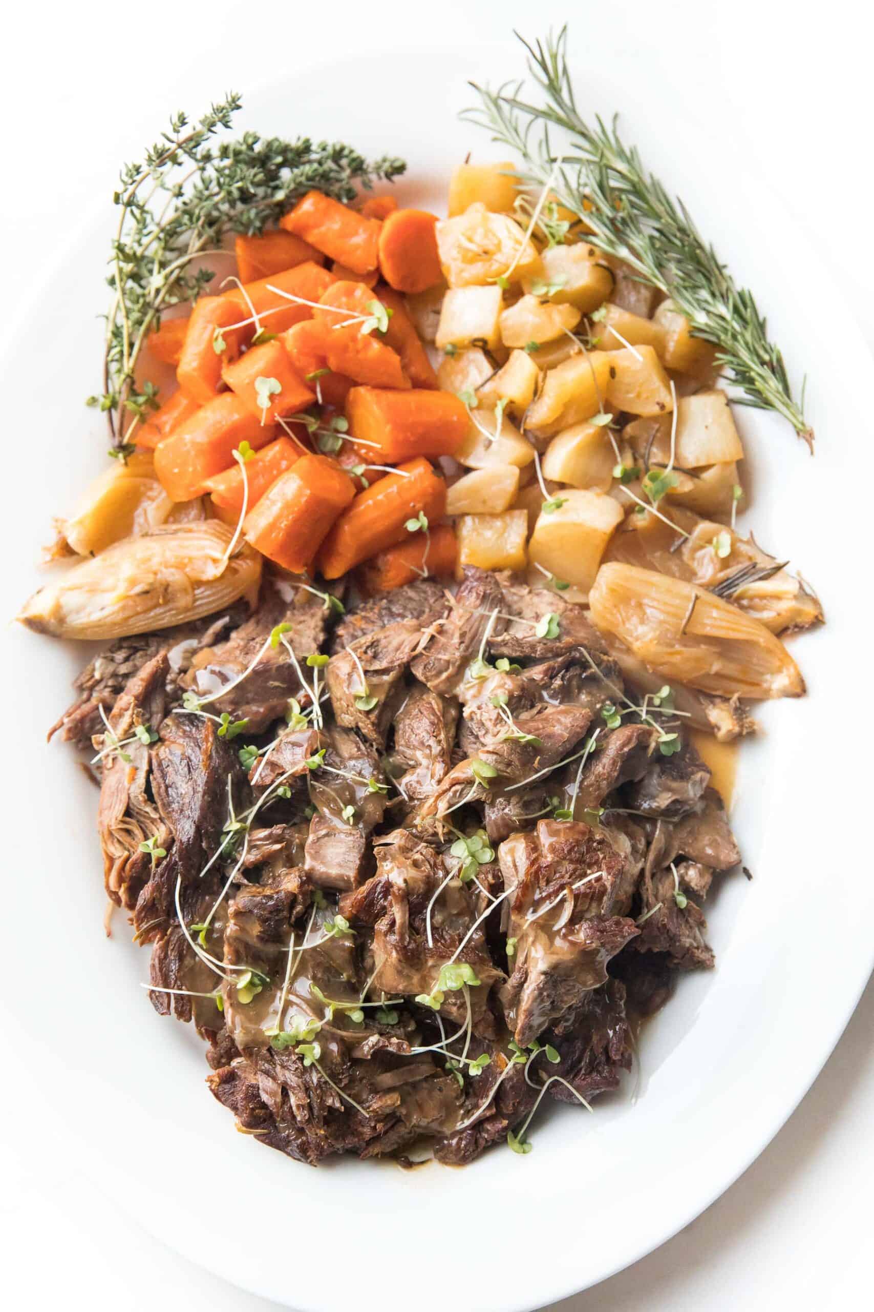 Pot roast + vegetables on a white plate with fresh herbs