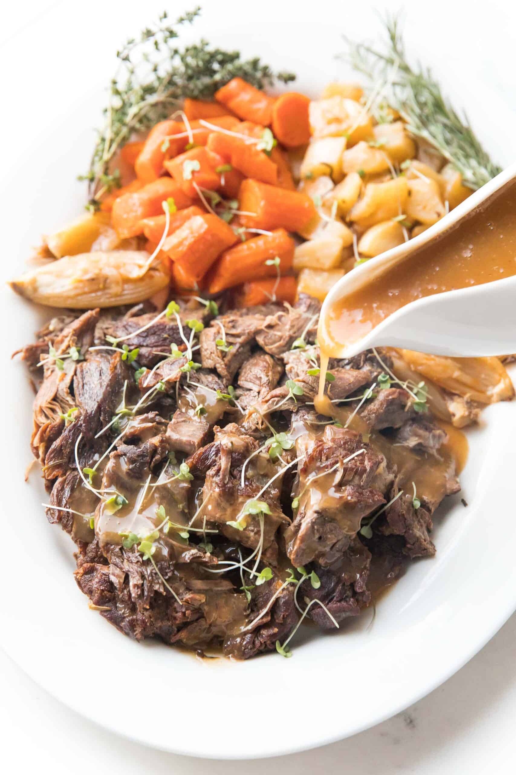 Pot roast + vegetables on a white plate with fresh herbs