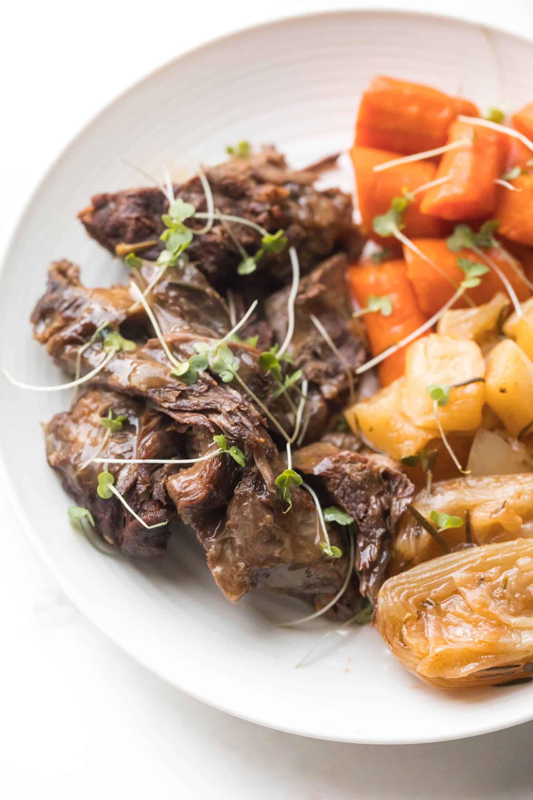 Pot roast + vegetables on a white plate with fresh herbs