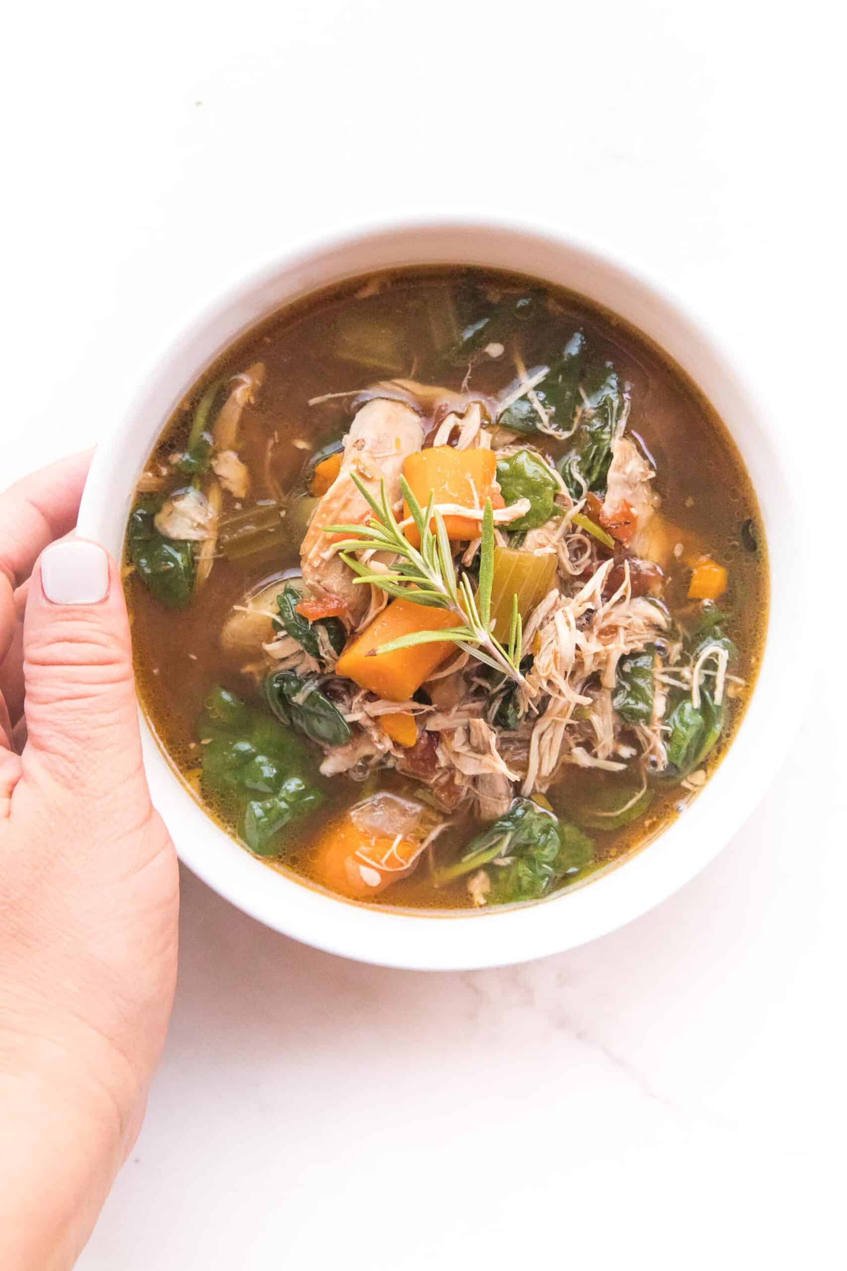 hand holding a bowl of tuscan chicken soup