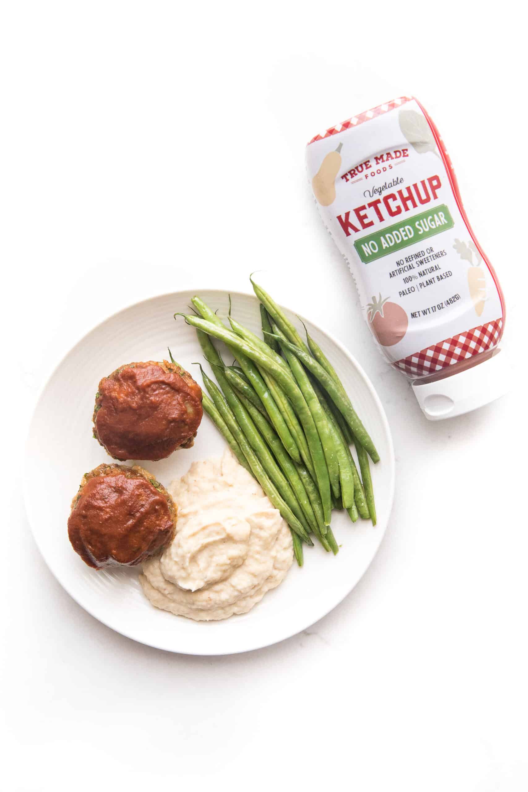 Mini meatloaf muffins topped with ketchup with green beans + mashed cauliflower + green beans on a white plate